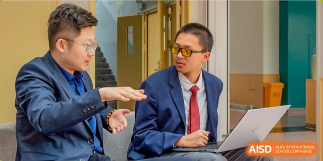 A male student from Suzhou Innovation Academy in a suit, red tie, and sunglasses seated while engaging in a discussion or presentation.