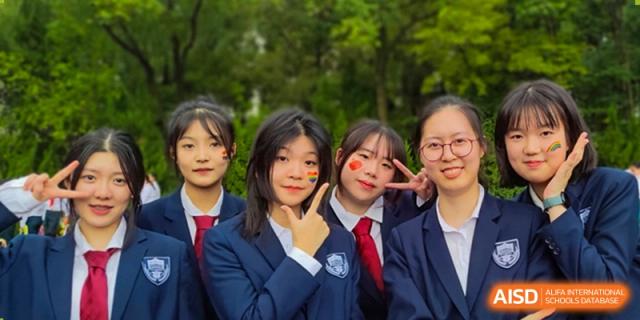 A group of smiling female Suzhou Innovation Academy students in school uniforms posing for a close-up photo outdoors, with painted hearts on their cheeks.