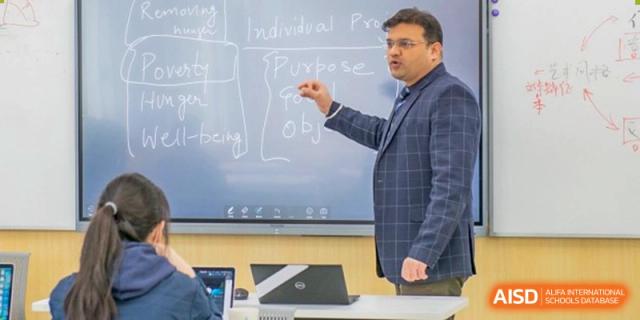 A male instructor at Suzhou Innovation Academy teaching a class, pointing to text on a whiteboard or screen.