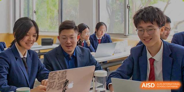 A male student from Suzhou Innovation Academy smiling while working on his laptop during a small group class.