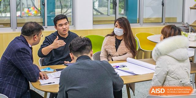 A small group of students and a teacher from Suzhou Innovation Academy having a focused discussion or meeting at a table.
