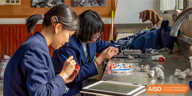 Two students from Suzhou Innovation Academy collaborating on a creative or technical project using small components and a tablet.