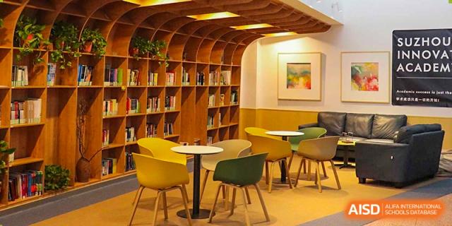 A stylish and modern student lounge or café area with curved wooden shelves, yellow chairs, and small tables at Suzhou Innovation Academy.