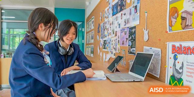 A female student from Suzhou Innovation Academy working on a laptop at a study desk covered with a colorful pinboard.