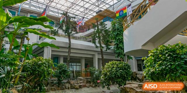 The modern, multi-story atrium or indoor garden area of Suzhou Innovation Academy, featuring trees, rocks, and natural light from a glass roof.