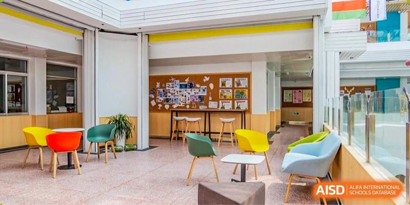 A bright, casual student common area with colorful chairs, a small table, and a bulletin board on a cork wall at Suzhou Innovation Academy.