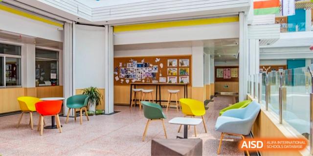 A bright, casual student common area with colorful chairs, a small table, and a bulletin board on a cork wall at Suzhou Innovation Academy.