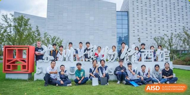 A group of Suzhou Innovation Academy students posing together outdoors in front of a modern grey building wall.