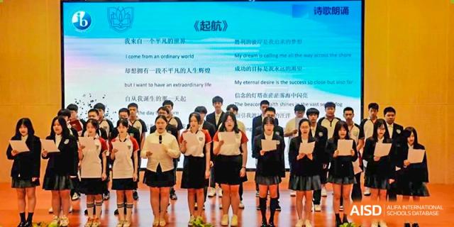 Suzhou Innovation Academy students in uniform reading text and lyrics projected on a screen during a choir or assembly performance.