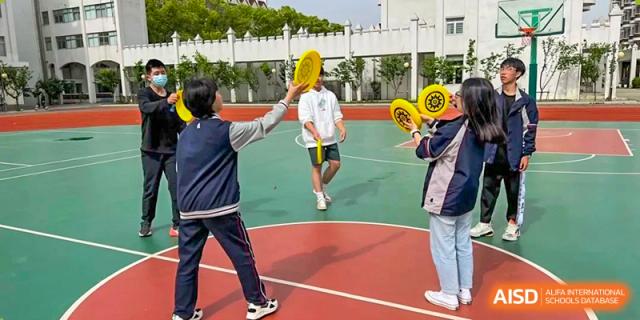 Two Suzhou Innovation Academy students playing a paddle or racquet game outdoors on a sports court.