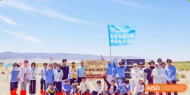 A group of cheering Suzhou Innovation Academy students posing outdoors with a banner under a bright blue sky, celebrating an achievement or event.