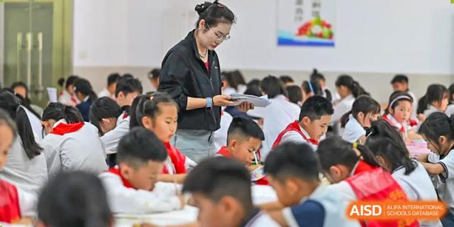 A female teacher assisting students at their desks during a class session at Walton International School Xuzhou.