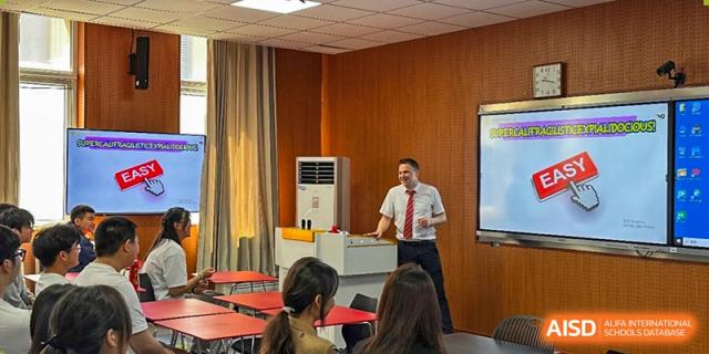 A male teacher giving a lecture or presentation to a class in a modern, wood-paneled room at Walton International School Xuzhou.