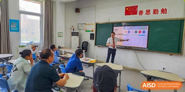 A male teacher leading a lesson from the front of the classroom at Walton International School Xuzhou with a chalkboard visible.