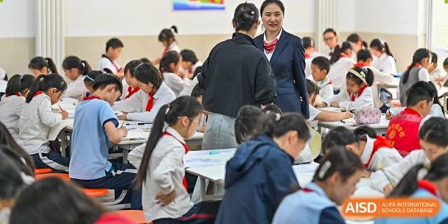 A female teacher or staff member speaking with a group of students in uniform at Walton International School Xuzhou.
