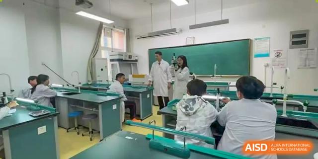 Students in lab coats conducting an experiment in a science laboratory with a teacher overseeing them at Walton International School Xuzhou.