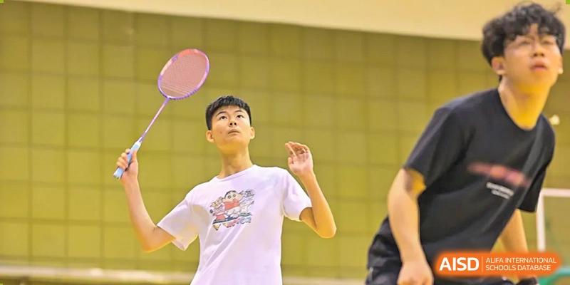 A student at Walton International School Xuzhou playing badminton, focused on hitting the shuttlecock during an indoor sports activity.