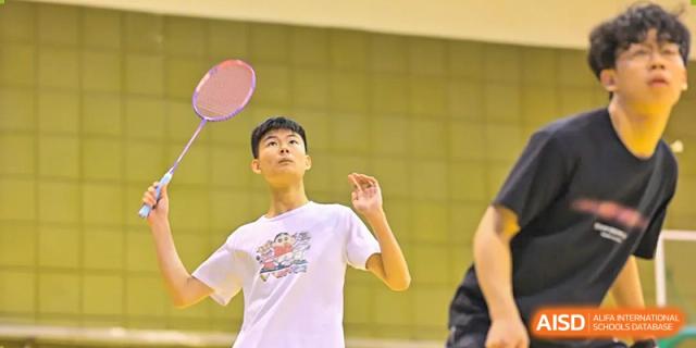 A student at Walton International School Xuzhou playing badminton, focused on hitting the shuttlecock during an indoor sports activity.