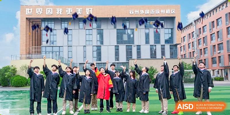 A group of graduating students at Walton International School Xuzhou in caps and gowns throwing their caps into the air in front of the main school building.