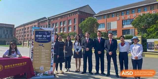A group of students and adult faculty members standing together for a photo in front of the main building of Walton International School Xuzhou.