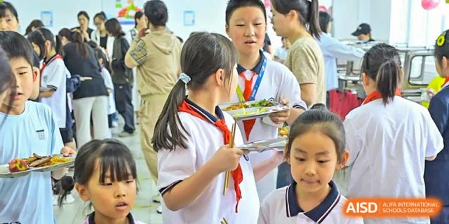 Two female students in uniform having a discussion while standing in the lunch line with their trays at Walton International School Xuzhou.