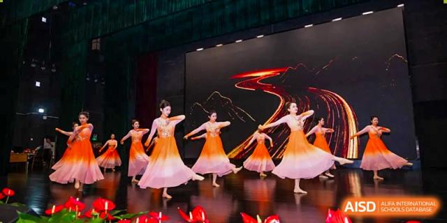 Students from Wuxi Huatian Bilingual School performing a beautiful, flowing dance on a stage with a dark background.