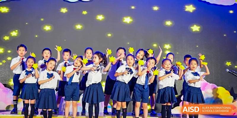 Happy young students from Wuxi Huatian Bilingual School in school uniforms smiling on a brightly lit stage.