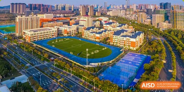 Aerial view of Wuxi Huatian Bilingual School campus complex with multiple buildings, a sports field, and track.