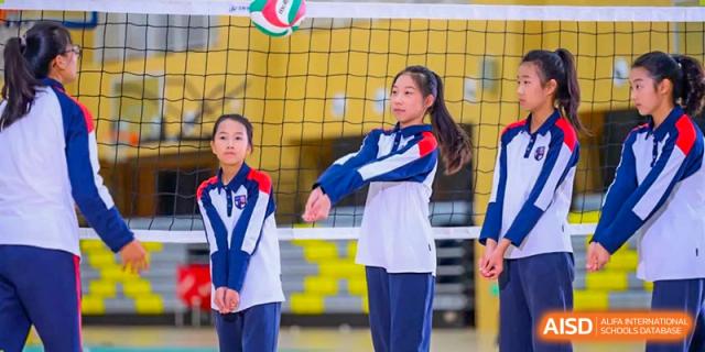 A female student from Wuxi Huatian Bilingual School in uniform playing volleyball and preparing to serve or bump the ball.