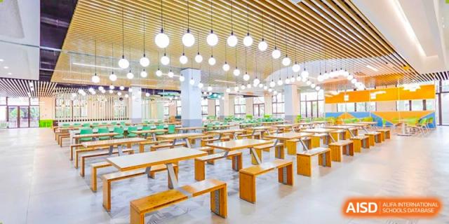 Large, brightly lit cafeteria or dining hall with wooden tables and benches at Wuxi Huatian Bilingual School.
