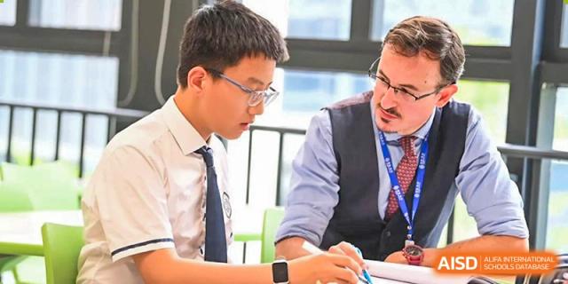 Wycombe Abbey School Hangzhou student in a white shirt and tie, wearing glasses, writing while seated next to an adult.