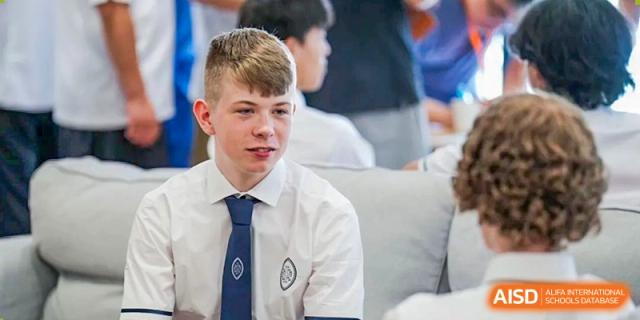 Wycombe Abbey School Hangzhou student with blonde hair, wearing a white shirt and school tie with the emblem, looking to the side.