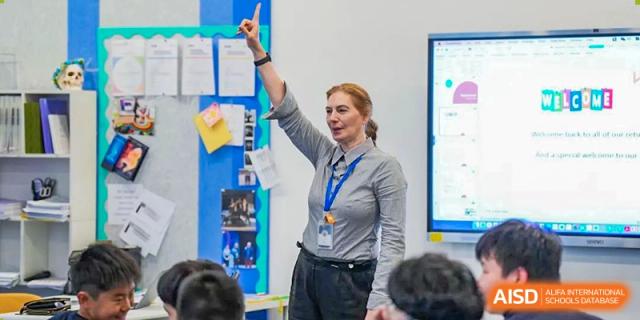 A female teacher at Wycombe Abbey School Hangzhou raising her hand in a classroom, with students seated.