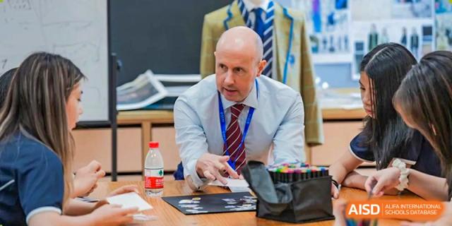 A male staff member or administrator at Wycombe Abbey School Hangzhou wearing a shirt and tie, seated at a desk and speaking.