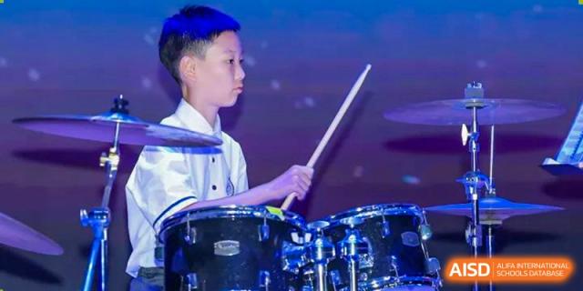 Young male student focused on playing the drums during a performance at Wycombe Abbey School Hangzhou.