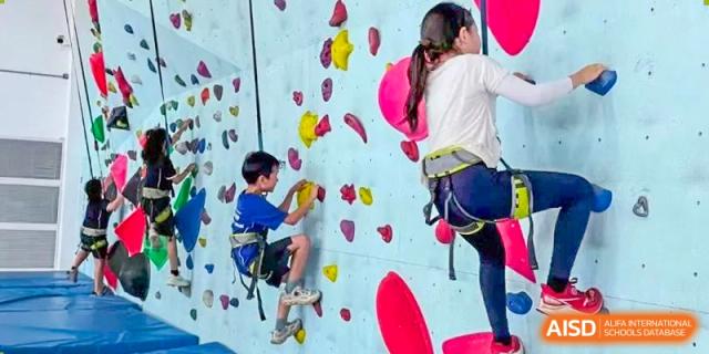 Students practicing rock climbing on an indoor wall with ropes and harnesses at Wycombe Abbey School Hangzhou.