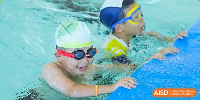 Two young students wearing goggles and caps receiving a swimming lesson in the pool at Wycombe Abbey School Hangzhou.