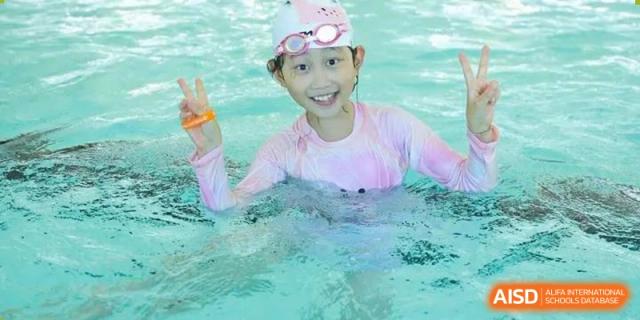 Young female student in the swimming pool, wearing a cap and goggles and smiling at the camera at Wycombe Abbey School Hangzhou.