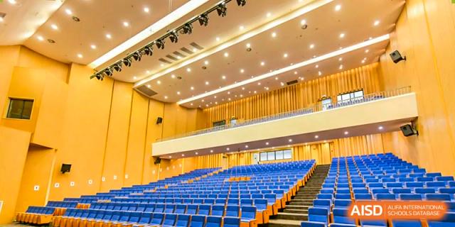 Interior of the spacious auditorium with rows of blue seating and a stage area at Wycombe Abbey School Hangzhou.