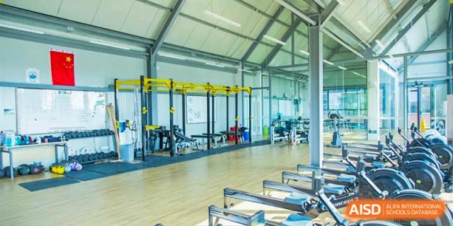 An interior view of the well-equipped Wycombe Abbey School Hangzhou gym or fitness center, showing rowing machines and yellow weight racks.
