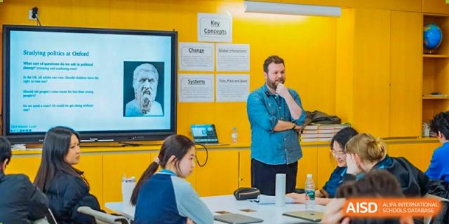 A male teacher at Xi'an Liangjiatan International School addresses students in a yellow-walled classroom.