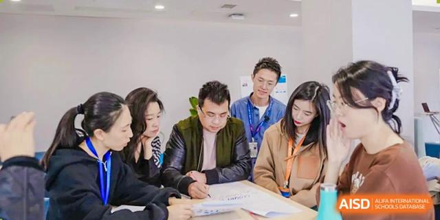 A diverse group of Xi'an Liangjiatan International School students and a teacher look at papers and discuss work around a table.