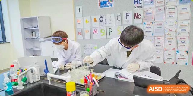 Two students from Xi'an Liangjiatan International School wearing lab coats work on a science experiment in a laboratory setting.