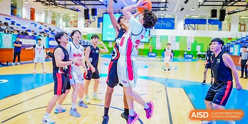 A student from Xi'an Liangjiatan International School in a pink and white jersey dribbles a basketball past a defender during a game.