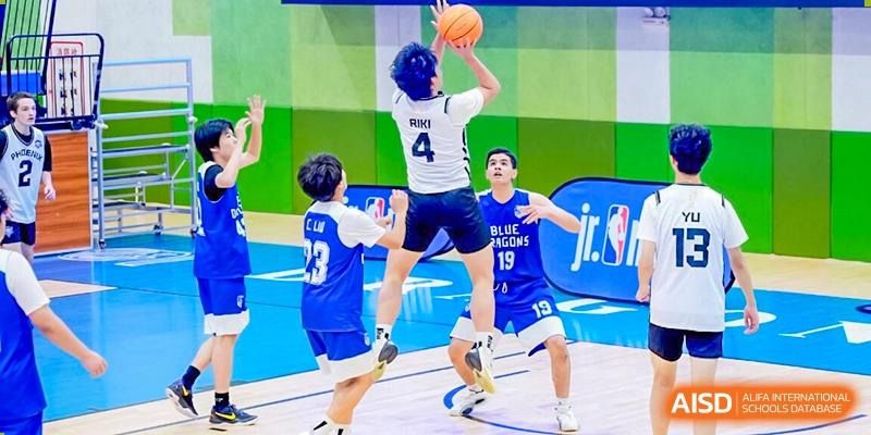 A player from Xi'an Liangjiatan International School wearing a blue and white jersey with the number 4 jumps high to take a shot over a defender during a competitive basketball game.