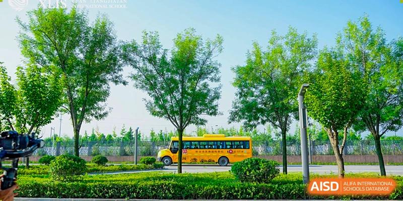 A bright yellow school bus for Xi'an Liangjiatan International School parked on a green lawn with trees and a blue sky in the background.