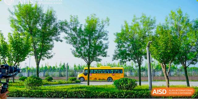 A bright yellow school bus for Xi'an Liangjiatan International School parked on a green lawn with trees and a blue sky in the background.