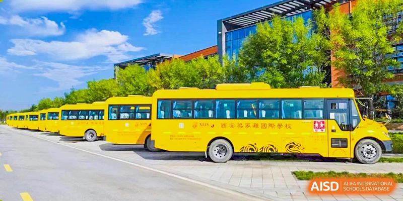 A yellow school bus for Xi'an Liangjiatan International School is parked outside a modern, glass-front school building on a sunny day.