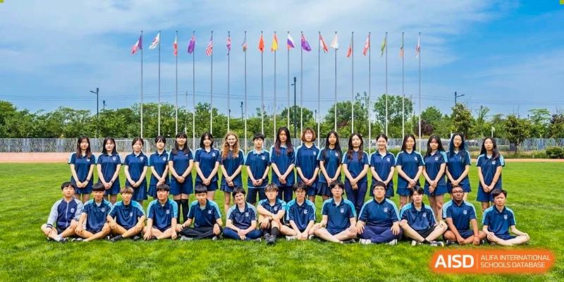 A large group of Xi'an Liangjiatan International School students and staff sit together in front of a row of international flags.