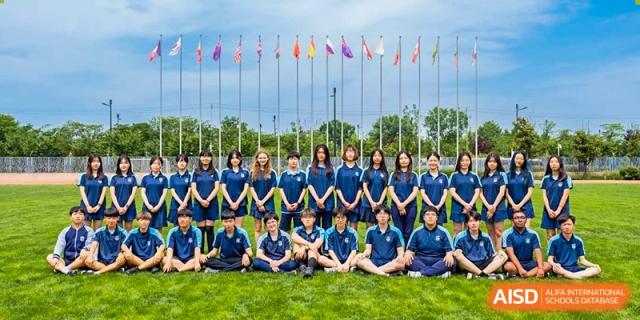 A large group of Xi'an Liangjiatan International School students and staff sit together in front of a row of international flags.